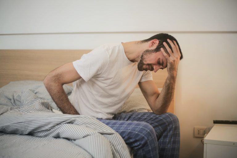 Homem sentado na cama com dor no corpo e cabeça