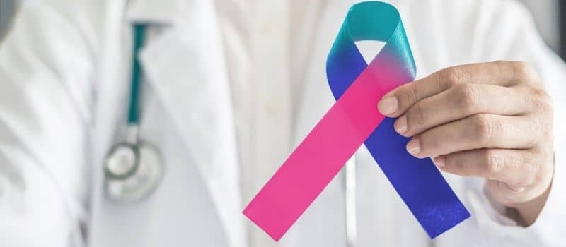 Médico segurando a fita do câncer azul e rosa